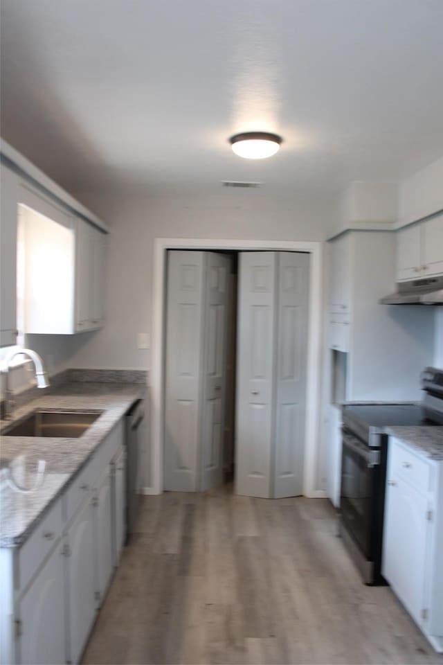 kitchen featuring white cabinetry, sink, stainless steel range with electric cooktop, light stone counters, and light wood-type flooring