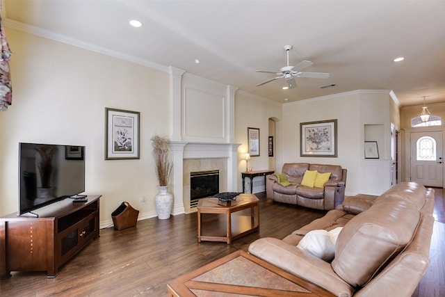 living room featuring a tiled fireplace, crown molding, dark hardwood / wood-style floors, and ceiling fan