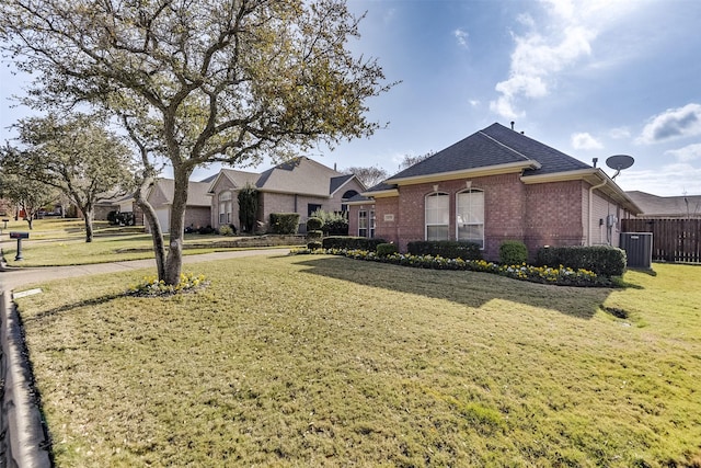 view of front of home with brick siding, roof with shingles, central AC, fence, and a front lawn