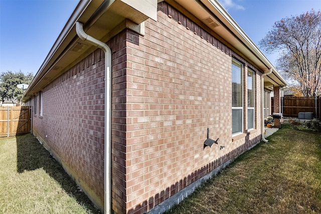 view of side of home featuring a yard, brick siding, and fence