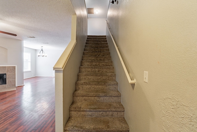 stairs featuring ceiling fan, hardwood / wood-style flooring, a tile fireplace, and a textured ceiling