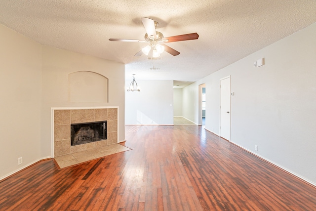 unfurnished living room featuring hardwood / wood-style floors, ceiling fan with notable chandelier, a fireplace, and a textured ceiling