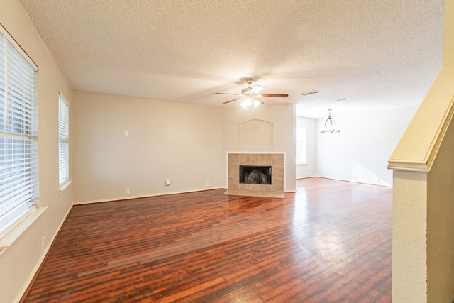 unfurnished living room featuring dark hardwood / wood-style floors, ceiling fan with notable chandelier, a tile fireplace, and a textured ceiling