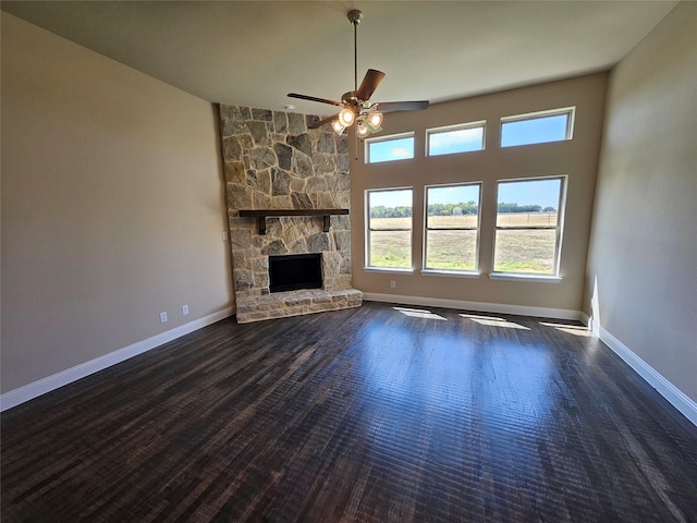 unfurnished living room with a high ceiling, dark hardwood / wood-style floors, a stone fireplace, and ceiling fan