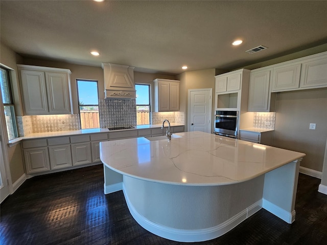 kitchen featuring white cabinets, stainless steel oven, tasteful backsplash, and an island with sink