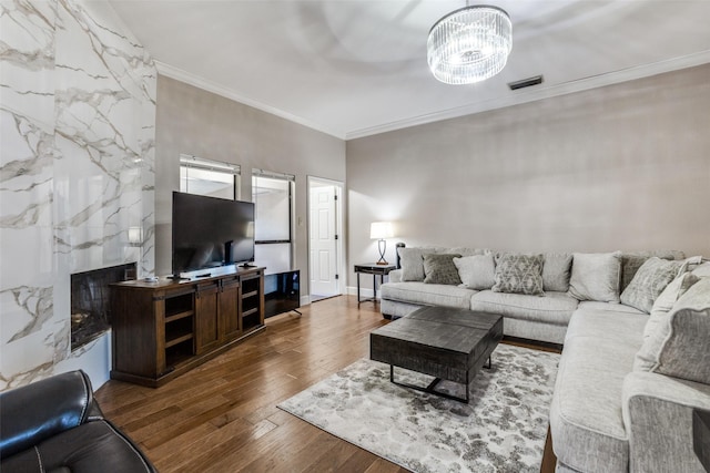 living room with wood-type flooring, crown molding, a high end fireplace, and an inviting chandelier