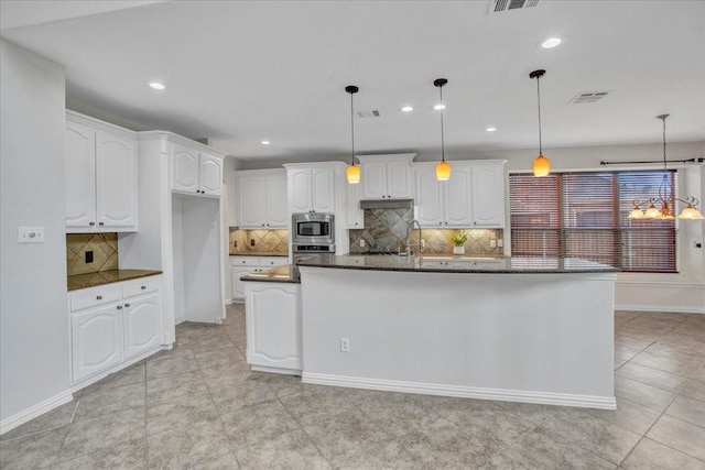 kitchen with appliances with stainless steel finishes, decorative light fixtures, white cabinetry, and a kitchen island with sink