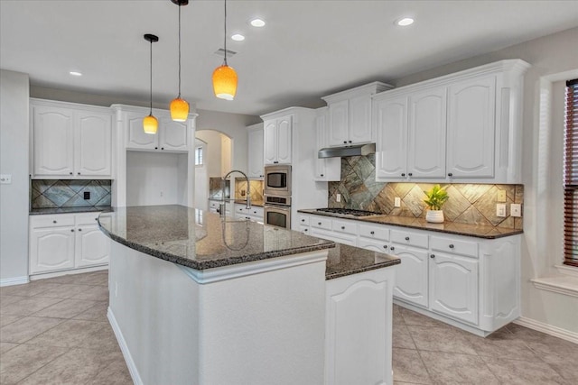 kitchen with pendant lighting, dark stone counters, an island with sink, appliances with stainless steel finishes, and white cabinetry