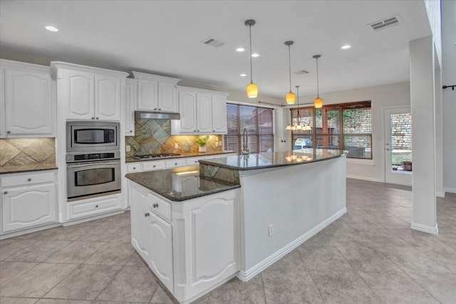 kitchen featuring a center island, dark stone counters, white cabinets, hanging light fixtures, and stainless steel appliances