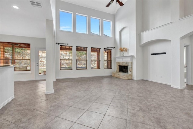 unfurnished living room featuring a stone fireplace, ceiling fan, light tile patterned floors, and a high ceiling