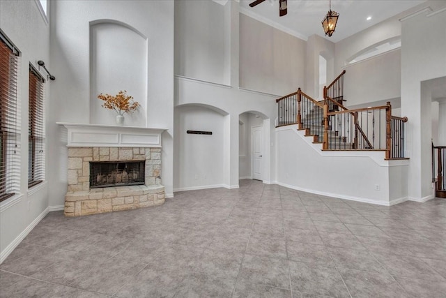 unfurnished living room with ceiling fan, a stone fireplace, a towering ceiling, and light tile patterned floors