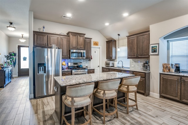 kitchen with hanging light fixtures, stainless steel appliances, light stone countertops, and a kitchen island