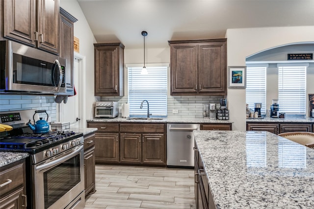 kitchen with lofted ceiling, dark brown cabinetry, sink, hanging light fixtures, and stainless steel appliances