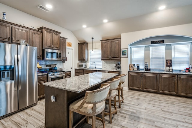 kitchen with pendant lighting, sink, lofted ceiling, appliances with stainless steel finishes, and a center island