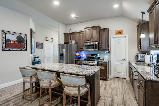 kitchen with stainless steel appliances, a center island, sink, and light stone countertops