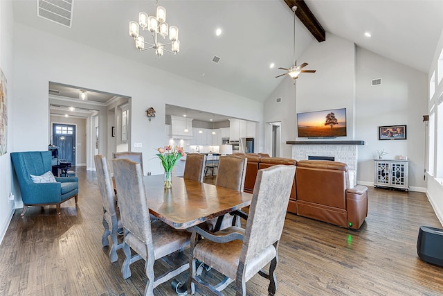 dining space featuring ceiling fan with notable chandelier, hardwood / wood-style flooring, beamed ceiling, and a stone fireplace