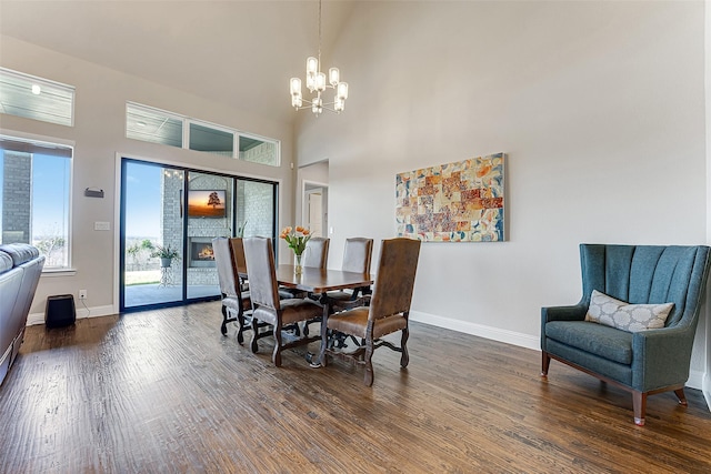 dining area with a towering ceiling, dark hardwood / wood-style flooring, a chandelier, and a stone fireplace