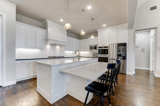 kitchen with stainless steel appliances, an island with sink, hanging light fixtures, a breakfast bar, and decorative backsplash