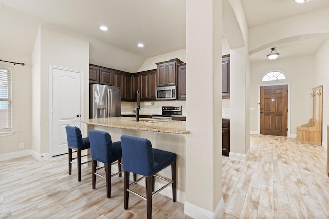 kitchen with appliances with stainless steel finishes, a breakfast bar, sink, light hardwood / wood-style floors, and light stone counters