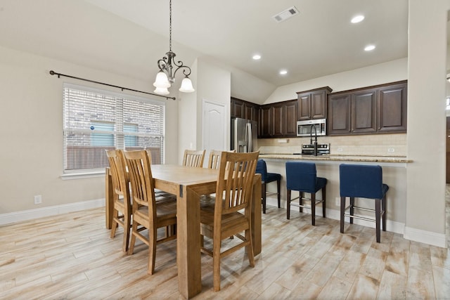 dining area with light hardwood / wood-style floors, lofted ceiling, and a notable chandelier