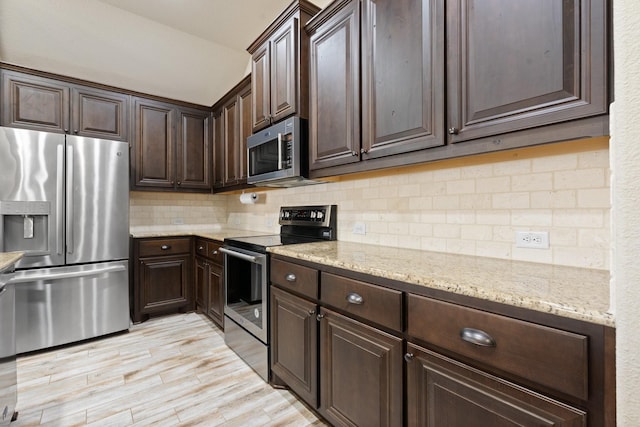 kitchen featuring appliances with stainless steel finishes, backsplash, dark brown cabinetry, light stone countertops, and light hardwood / wood-style floors