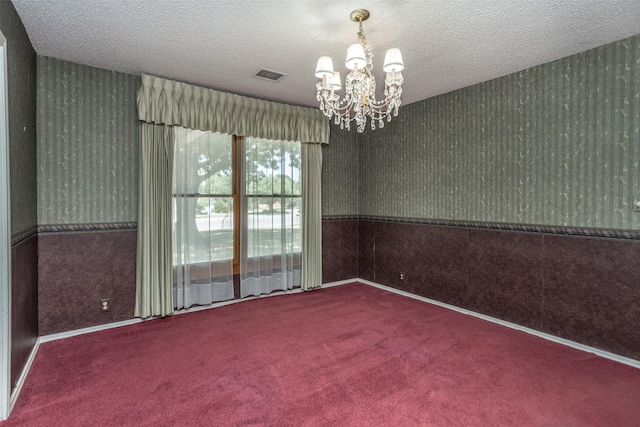 spare room with carpet flooring, a textured ceiling, and an inviting chandelier