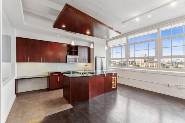 kitchen with appliances with stainless steel finishes, dark hardwood / wood-style flooring, a kitchen island with sink, and decorative backsplash