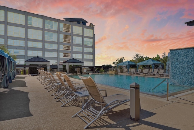 pool at dusk featuring a gazebo and a patio