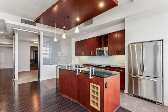 kitchen featuring hardwood / wood-style floors, pendant lighting, a center island with sink, decorative backsplash, and stainless steel appliances