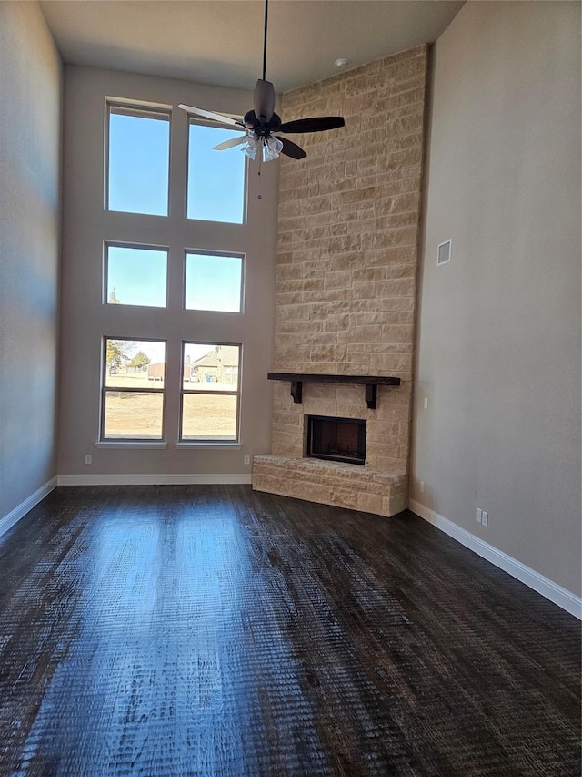 unfurnished living room with ceiling fan, a towering ceiling, and a fireplace