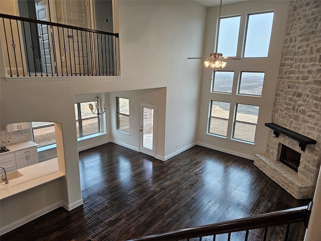 living room featuring ceiling fan, a stone fireplace, dark hardwood / wood-style flooring, and a towering ceiling