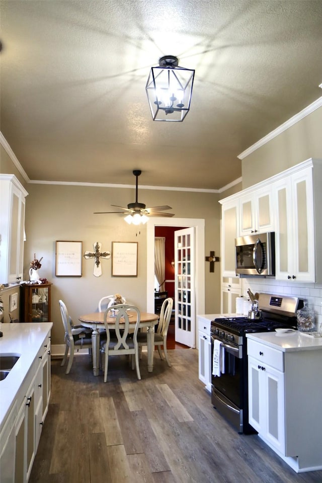 kitchen with crown molding, dark wood-type flooring, appliances with stainless steel finishes, backsplash, and white cabinets