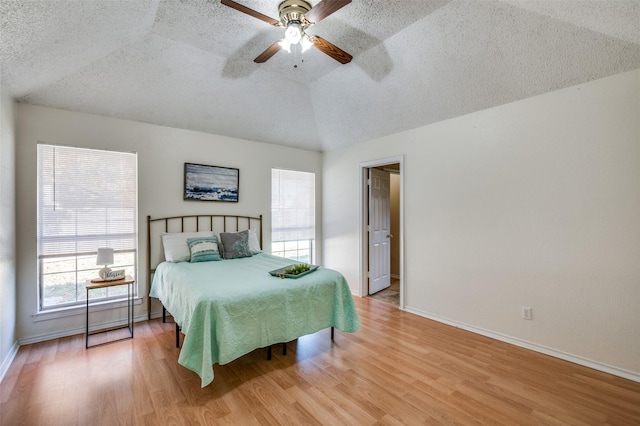 bedroom with ceiling fan, light wood-type flooring, a textured ceiling, and lofted ceiling