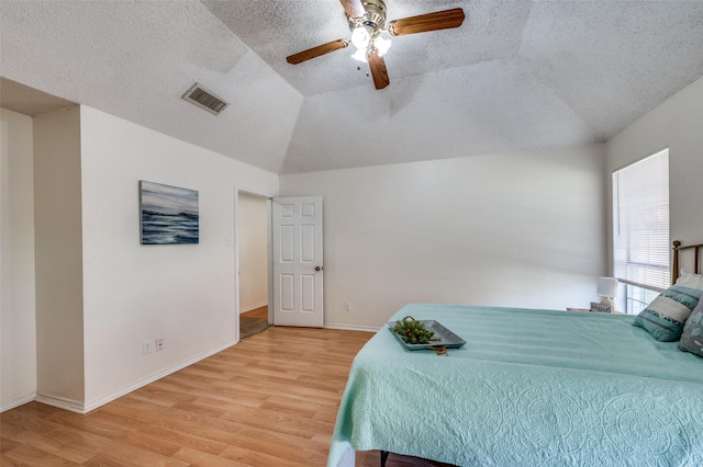 bedroom with ceiling fan, light wood-type flooring, a textured ceiling, and lofted ceiling