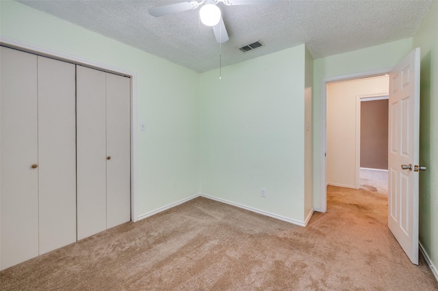 unfurnished bedroom featuring a textured ceiling, ceiling fan, light carpet, and a closet