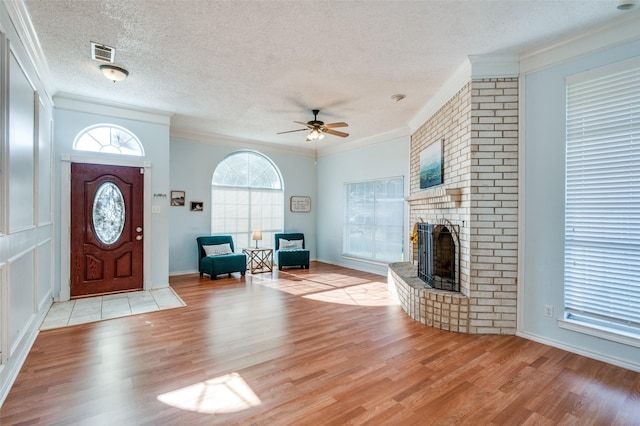 foyer with crown molding, ceiling fan, a fireplace, a textured ceiling, and light wood-type flooring