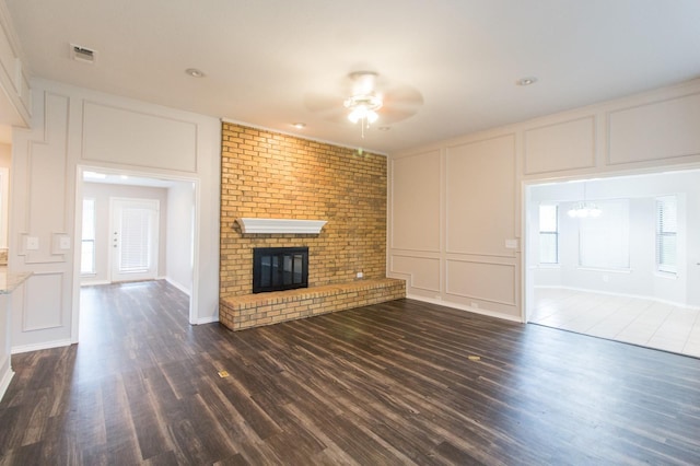 unfurnished living room featuring ceiling fan with notable chandelier, dark hardwood / wood-style floors, a brick fireplace, and brick wall