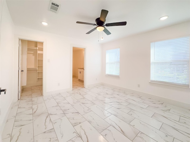 unfurnished bedroom featuring multiple windows, a walk in closet, a closet, and ceiling fan