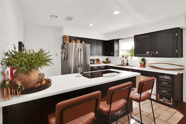 kitchen featuring stainless steel refrigerator, dishwasher, sink, a kitchen bar, and decorative backsplash