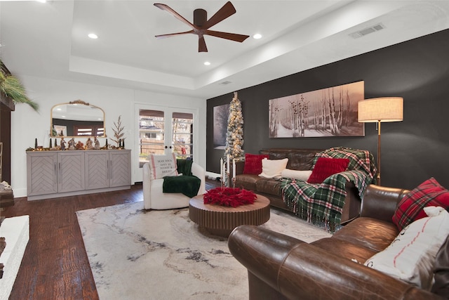 living room with ceiling fan, dark wood-type flooring, and a tray ceiling