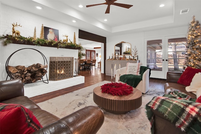 living room featuring ceiling fan, french doors, a raised ceiling, wood-type flooring, and a fireplace