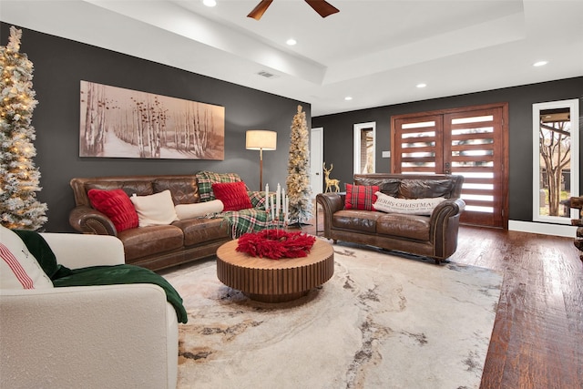 living room featuring ceiling fan, a raised ceiling, and wood-type flooring