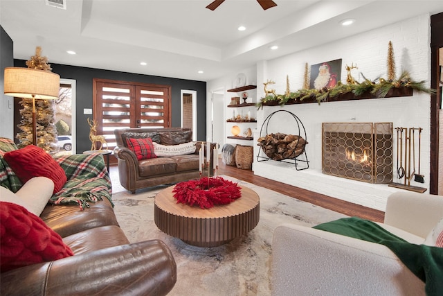 living room featuring ceiling fan, light hardwood / wood-style floors, a raised ceiling, and a fireplace