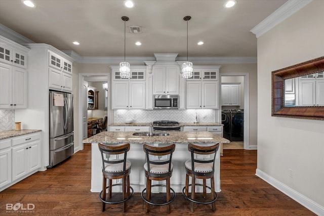 kitchen with pendant lighting, appliances with stainless steel finishes, white cabinetry, light stone countertops, and an island with sink