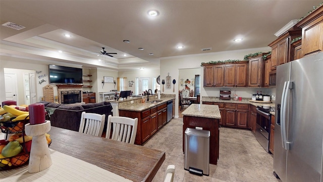 kitchen with appliances with stainless steel finishes, light stone counters, ornamental molding, a kitchen island with sink, and ceiling fan