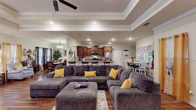 living room featuring ceiling fan with notable chandelier, ornamental molding, and dark wood-type flooring