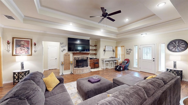 living room with a tray ceiling, crown molding, a fireplace, and wood-type flooring