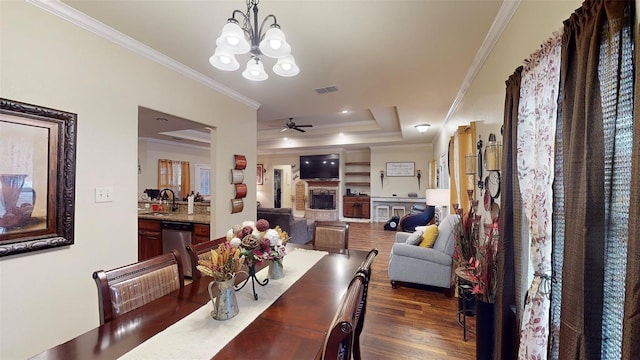 dining area with dark wood-type flooring, ceiling fan with notable chandelier, a raised ceiling, sink, and ornamental molding