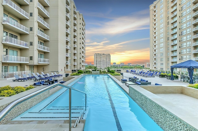 pool at dusk featuring a gazebo and a patio area