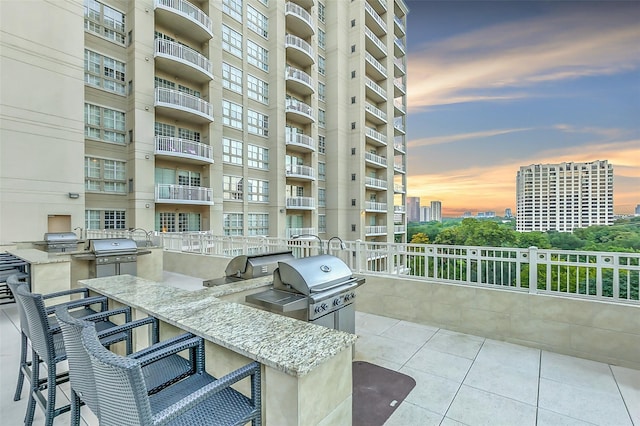 patio terrace at dusk featuring a grill, exterior bar, and exterior kitchen